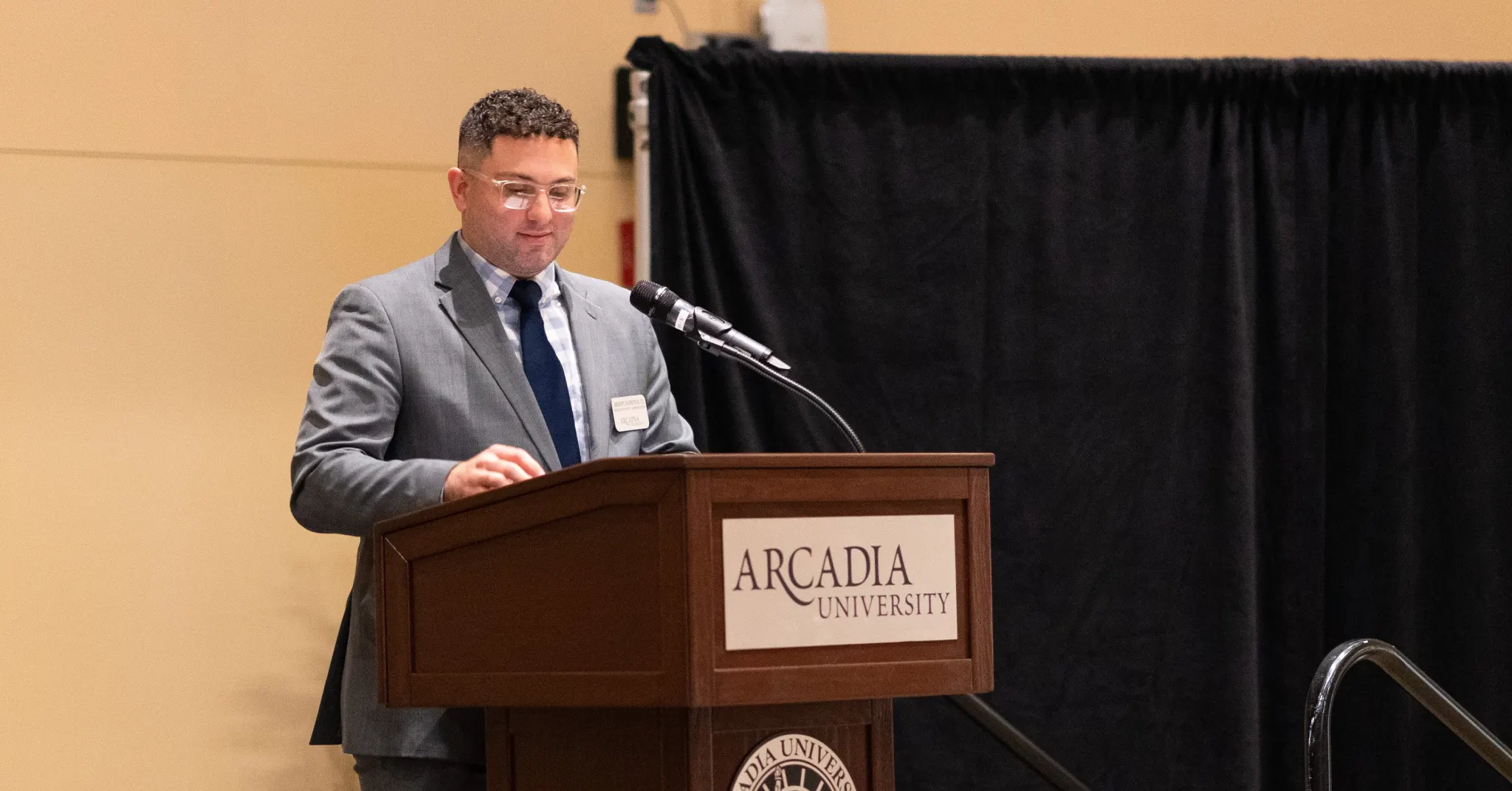 man in suit standing behind Arcadia University branded podium in the Kuch Center during the Athletic Award Event