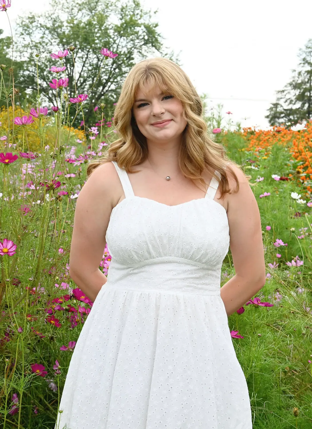 Kylee Kramer in a white dress posing with a field of flowers behind her.