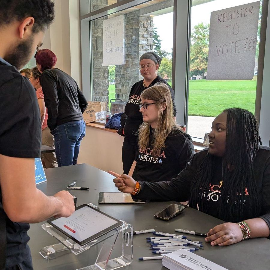 students wearing Arcadia Votes t-shirts sit at a table in the Chat registering students to vote