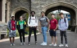 Six students stand together outside on campus while smiling at the camera.