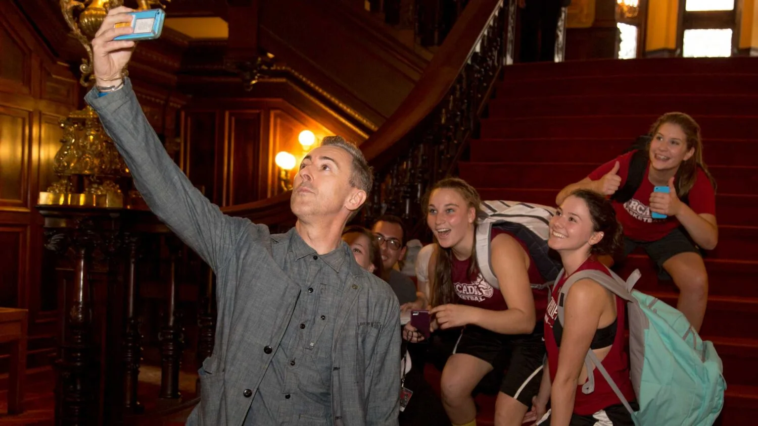 Alan Cumming takes selfie with group of Arcadia students smiling in the background.