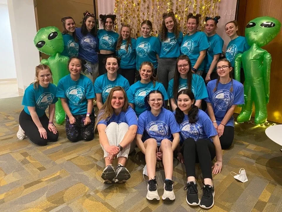 A group of students in three rows wears matching blue t-shirts