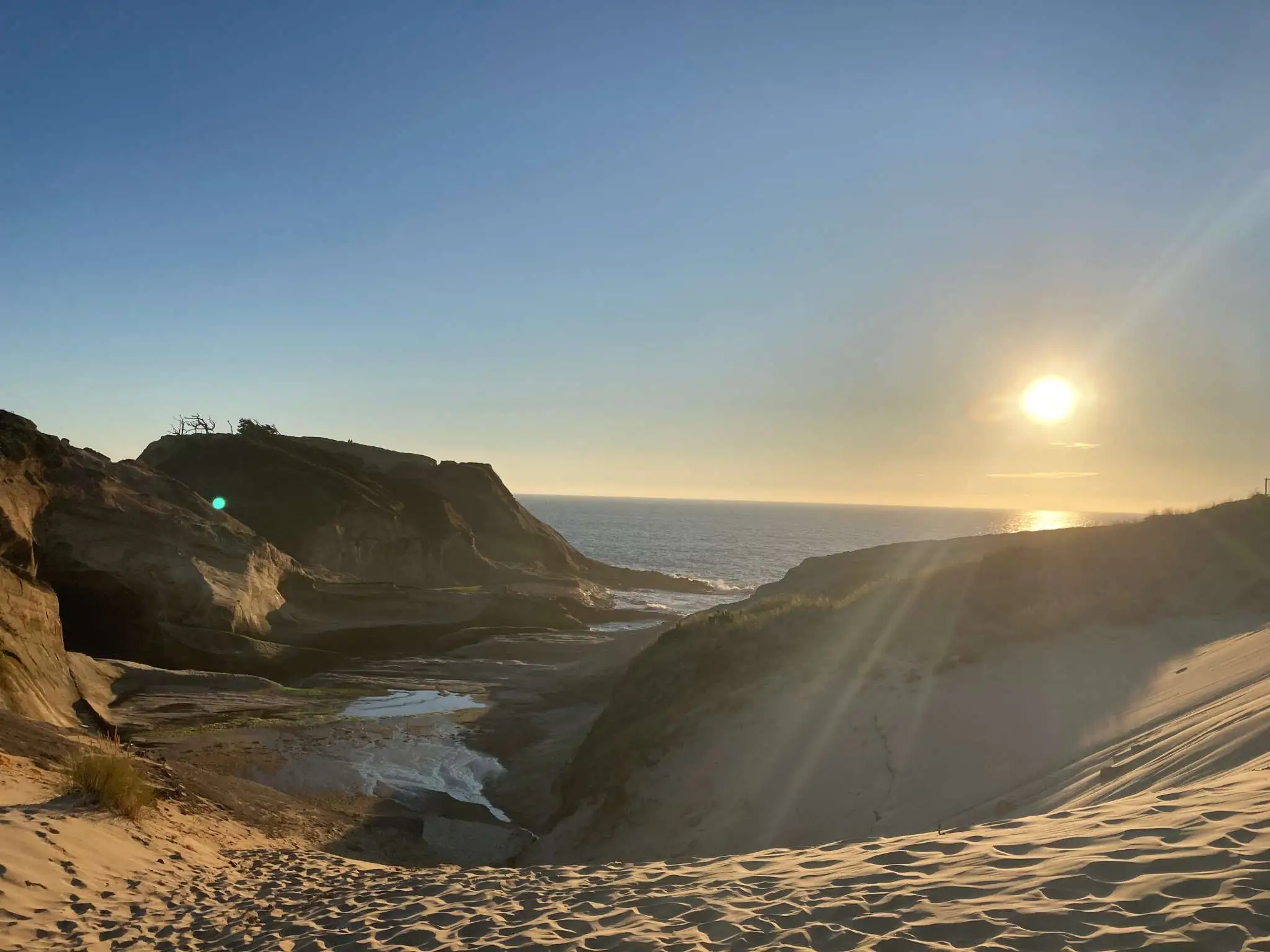 The sun shines low over the horizon over beach dunes by a body of water