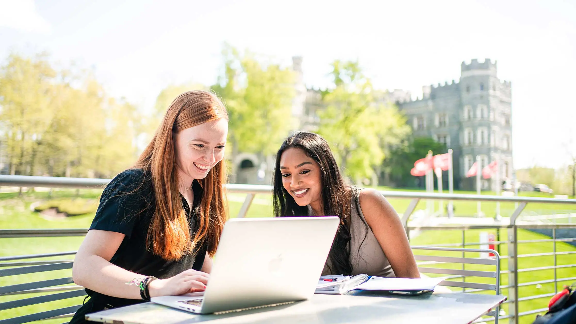 Two students sitting on the Commons balony studying together and looking at an Apple laptop