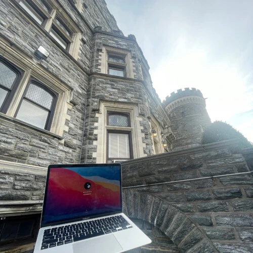 A laptop being held up next to Grey Towers Castle.