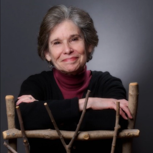 An older woman with a warm smile in a dark pink turtleneck and black sweater