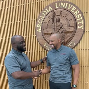 Eugene Garmon (left) and Dr. Donavan McCargo (right) shaking hands in front of the Arcadia University seal.